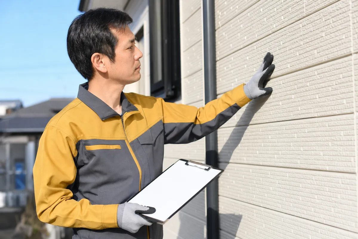 チェックシートを手に外壁を点検するスタッフ